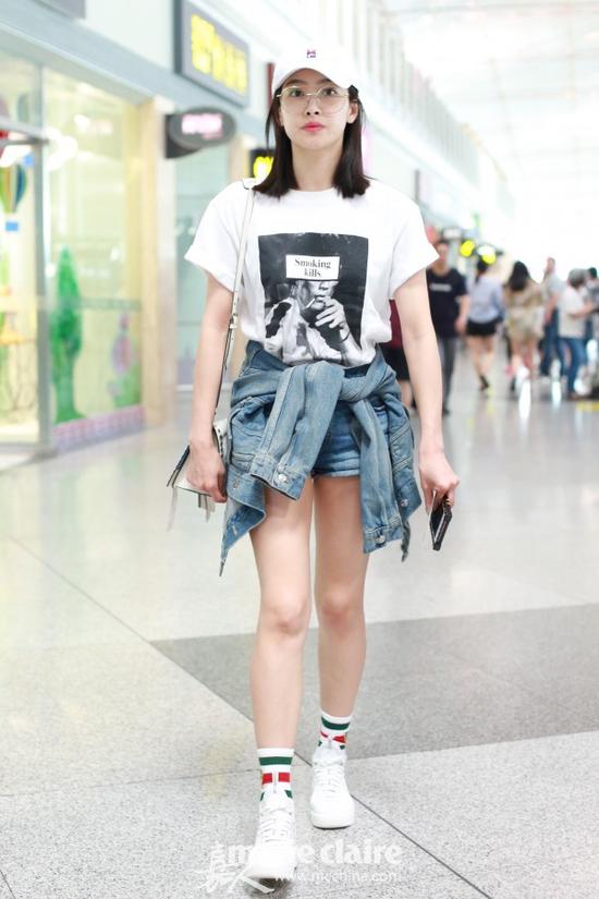 宋茜机场街拍。她头戴白色印花鸭舌帽,戴金丝边圆框眼镜,身穿白色印花T恤,肩背Prada白色圆钉镶嵌手袋,手拿Louis Vuitton棕色老花手机壳,下穿蓝色牛仔短裤,系蓝色牛仔夹克,脚踩Nike白色网面拼接球鞋,内搭Gucci拼色条纹虎头刺绣短袜。