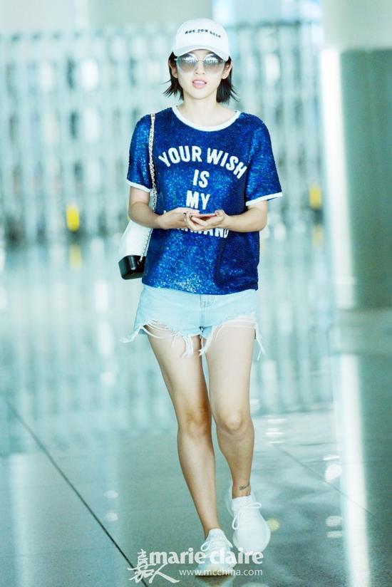 唐艺昕机场街拍。她戴黑色字母刺绣白色棒球帽,戴圆框墨镜,身穿宝蓝色亮片T恤,下身穿不顾子毛边牛仔短裤,脚踩Yeezy白色运动鞋,肩背Chanel黑白拼色链条双肩包。