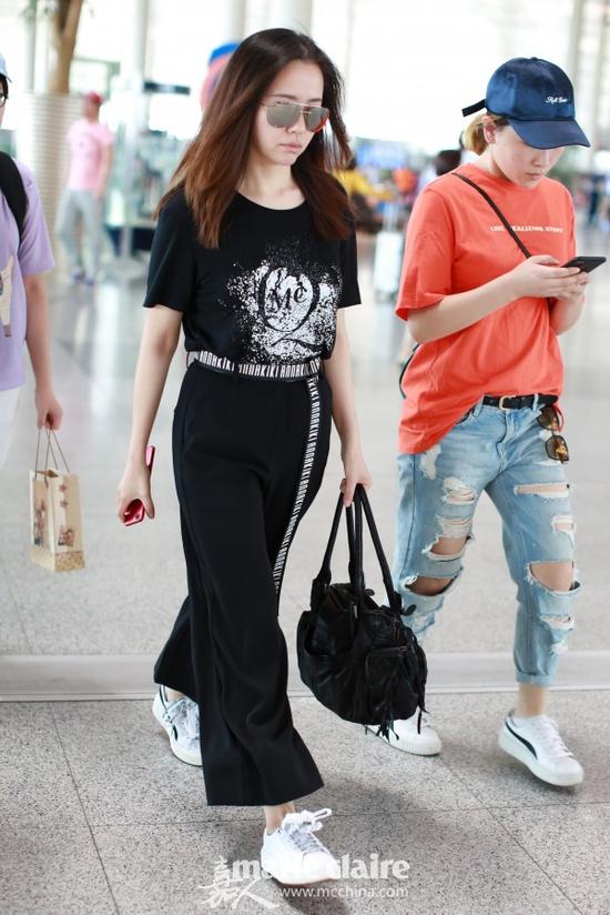 张靓颖机场街拍。她戴镜面墨镜,身穿白色印花Alexander McQueen黑色T恤,下穿黑色阔腿裤,搭配黑白字母腰带,脚踩Puma白色球鞋,手提黑色包袋